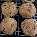 Nine chocolate chip cookies cooling on a wire rack over a black surface.